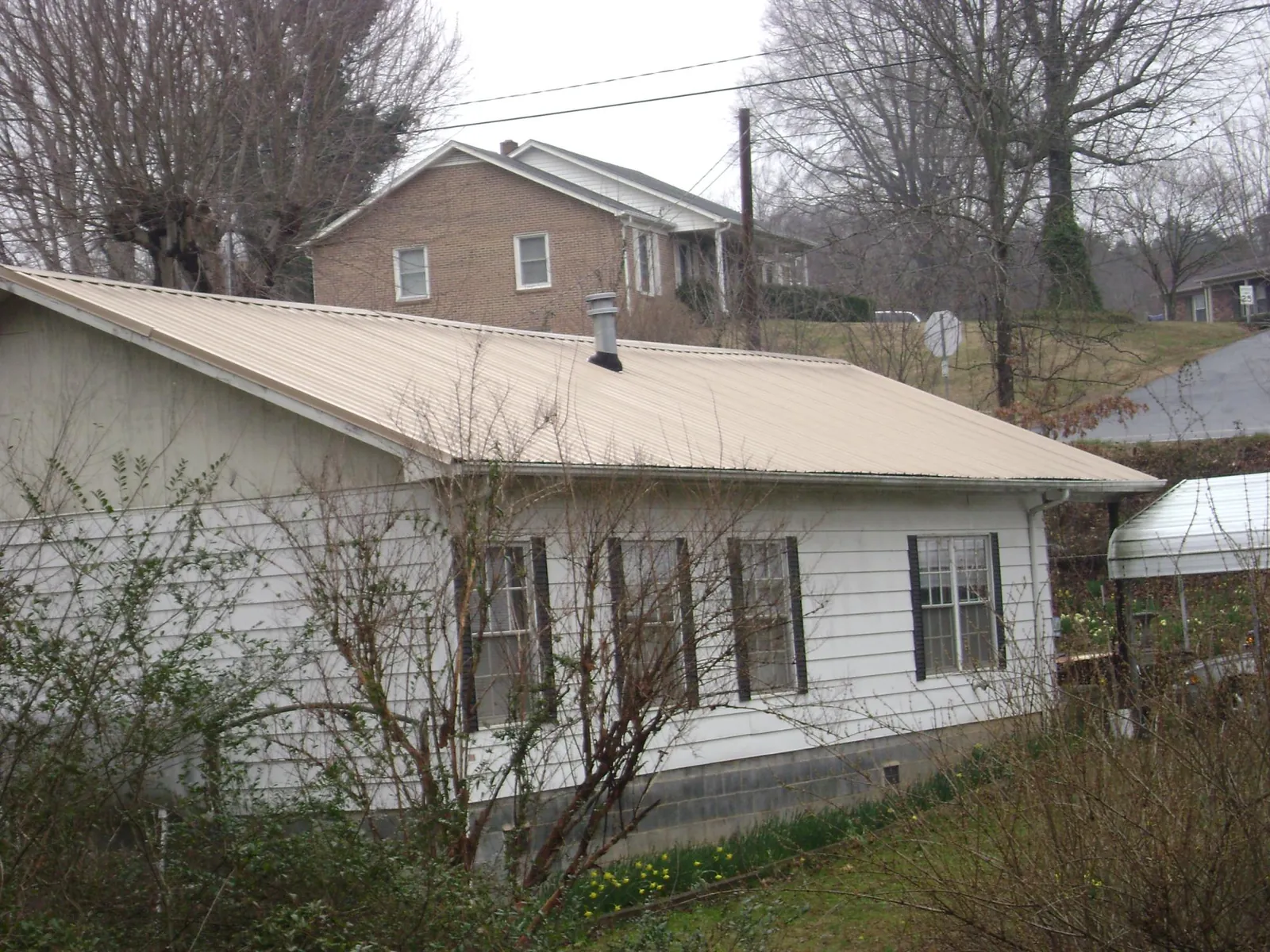 Tan metal roof on a white sided house set into a hillside — Commercial Roofing by Roofing Brothers in Shiloh